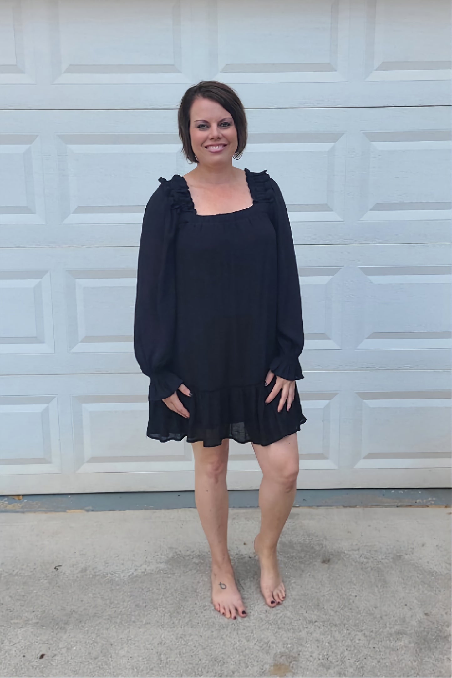 You'll look and feel beautiful in our new Black Mini Dress! This mini-length dress features a square neckline, long sleeves with elastic at the wrist, tiered hemline, back tie, ruffle detail, and it is lined.