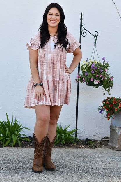 You will surely want this adorable dress among your clothes with its soft, lightweight breezy material and a mauve and white tie dye pattern. This dress features a scooped neckline, short ruffle sleeves and an ultra relaxed tiered silhouette that falls into an uneven lower-thigh length hemline.
